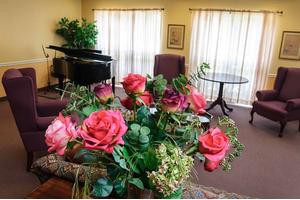 A cozy living room with a bouquet of roses, a grand piano, and comfortable seating.