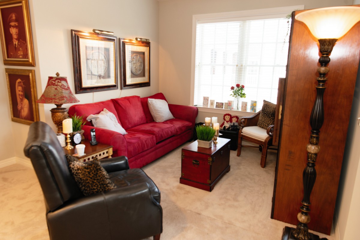 A cozy living room with a red sofa, armchairs, and a coffee table, warmly lit by natural light from a large window.