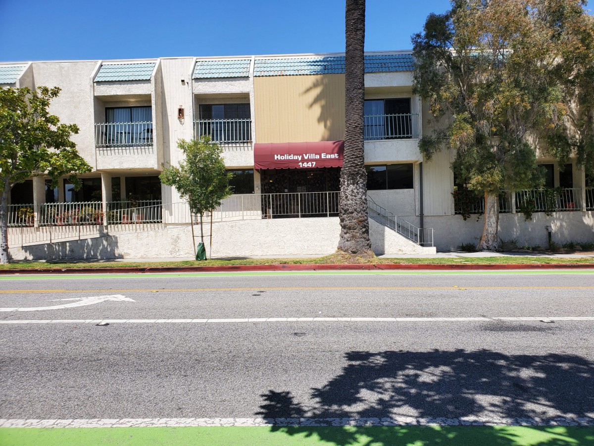 A street view of a building with an awning and palm trees on a sunny day.