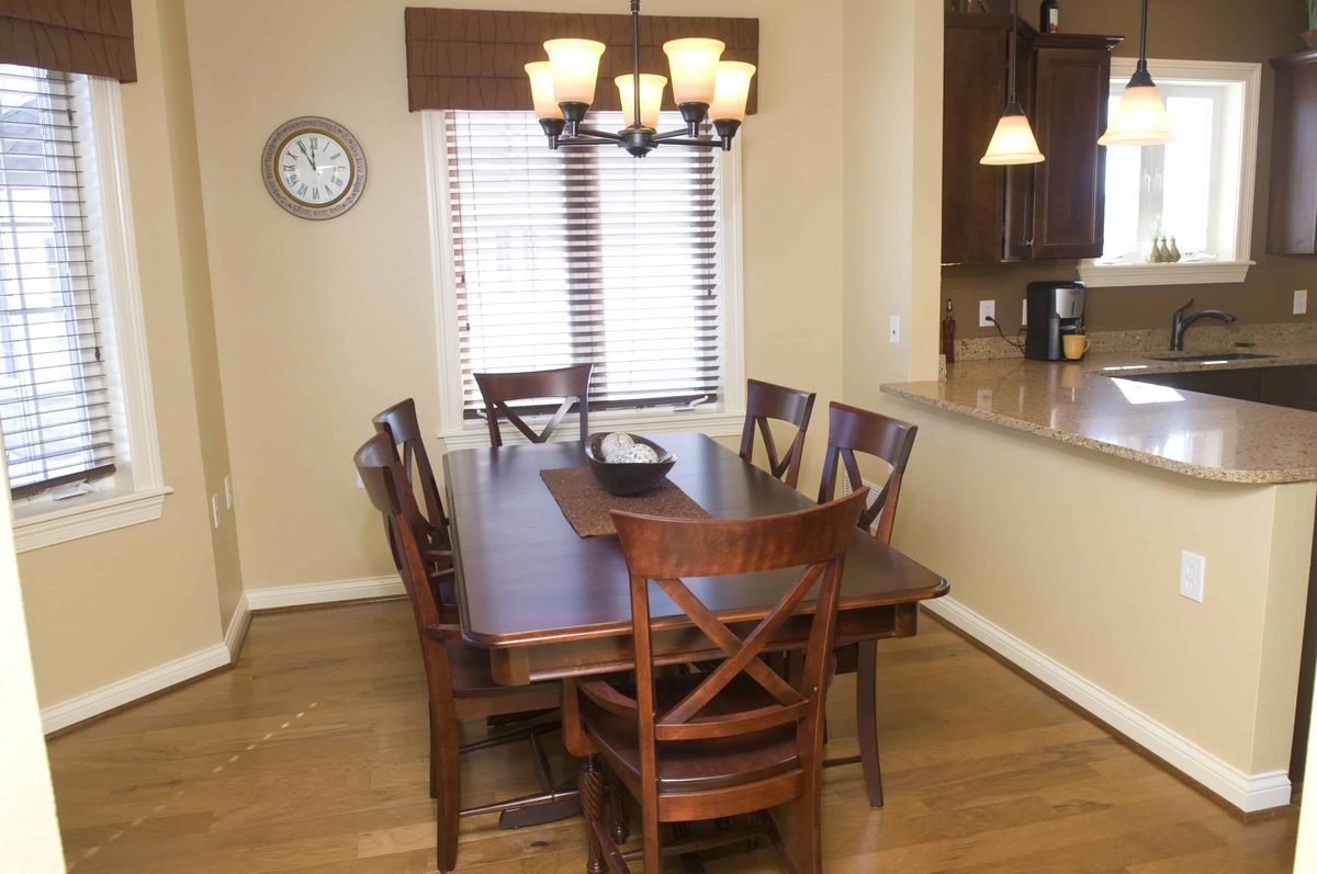 A dining room featuring a wooden table with six chairs and a chandelier, next to a window with blinds.