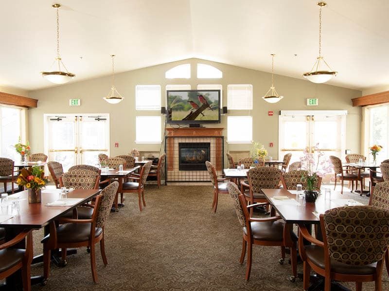 A spacious dining area with multiple tables and chairs, featuring a fireplace and large windows.
