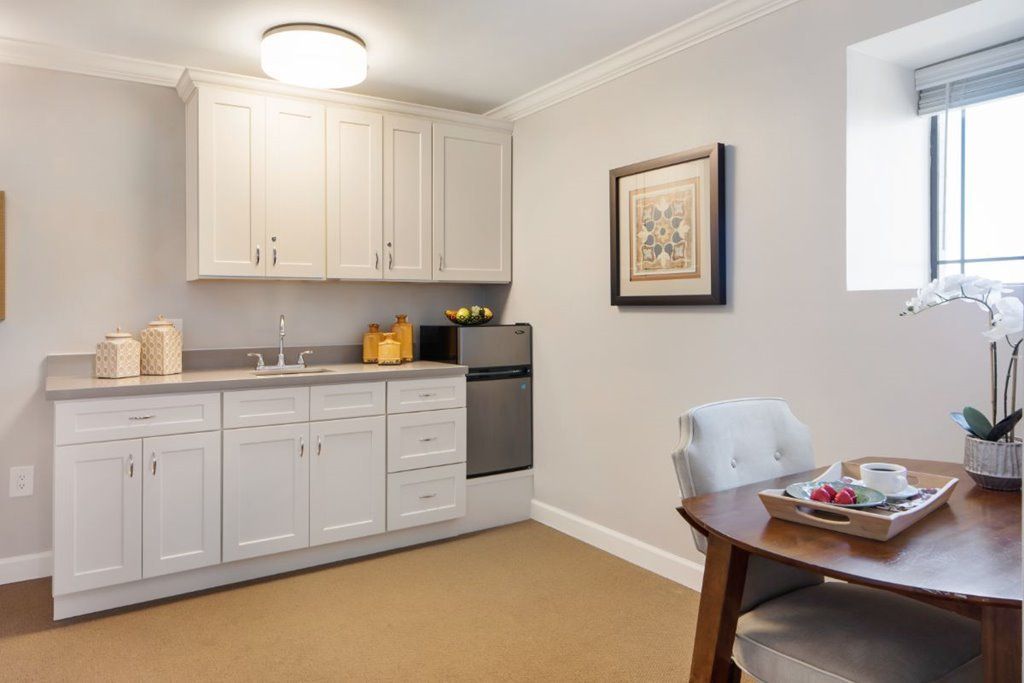 Compact kitchenette with white cabinets, a mini fridge, and a small dining area.