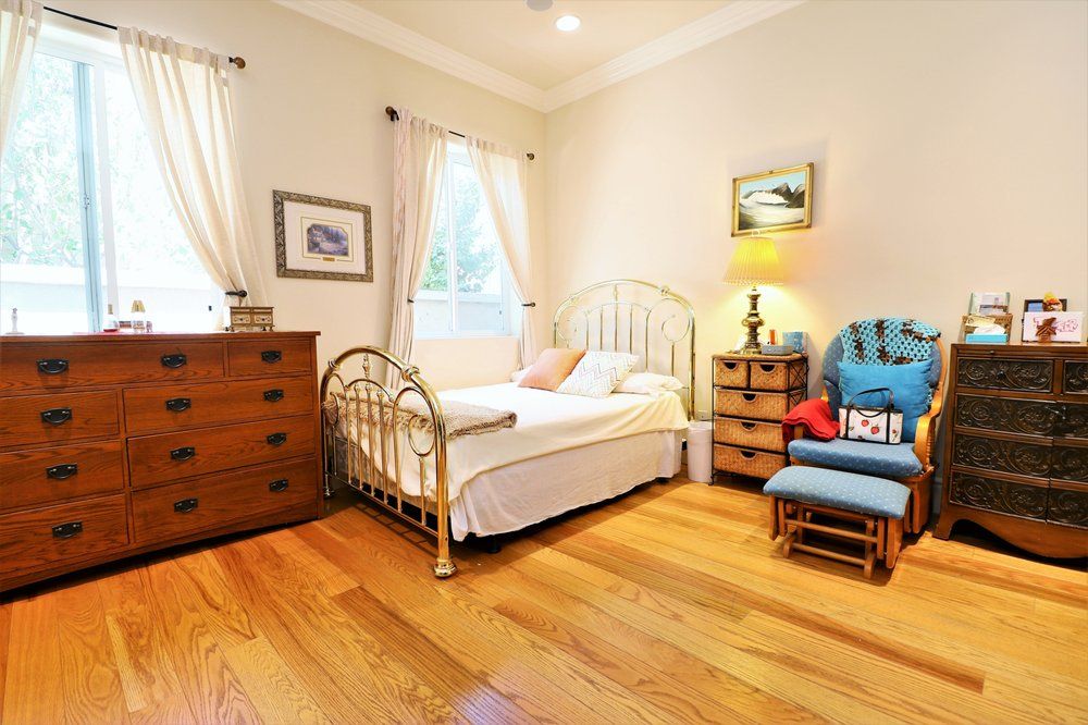 A cozy bedroom with a metal-frame bed, a wooden dresser, and a comfortable chair on a hardwood floor.