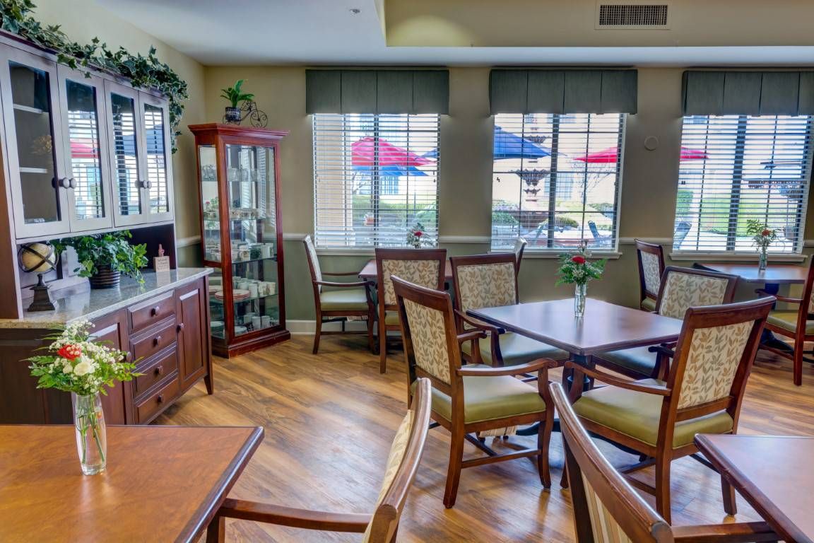 A cozy dining area with wooden tables and chairs, illuminated by natural light from large windows.