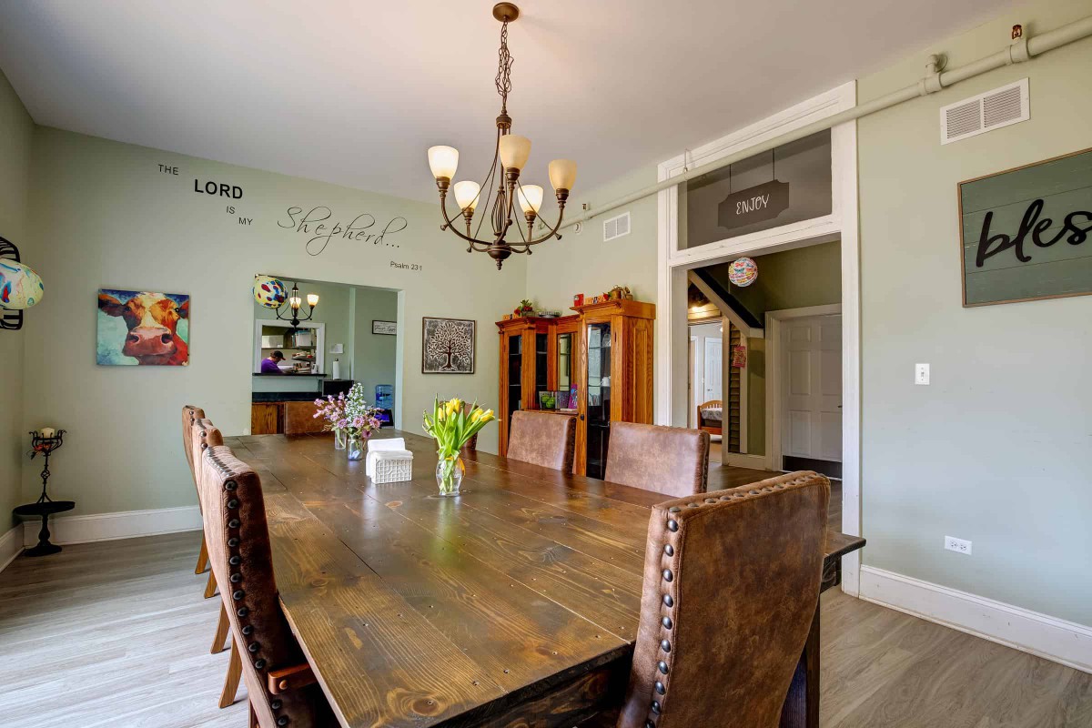 A cozy dining room featuring a large wooden table, leather chairs, and a decorative chandelier.
