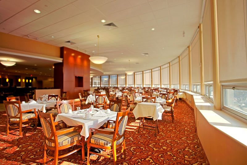 An elegant restaurant dining area with neatly arranged tables and chairs, featuring large windows and a warm ambiance.