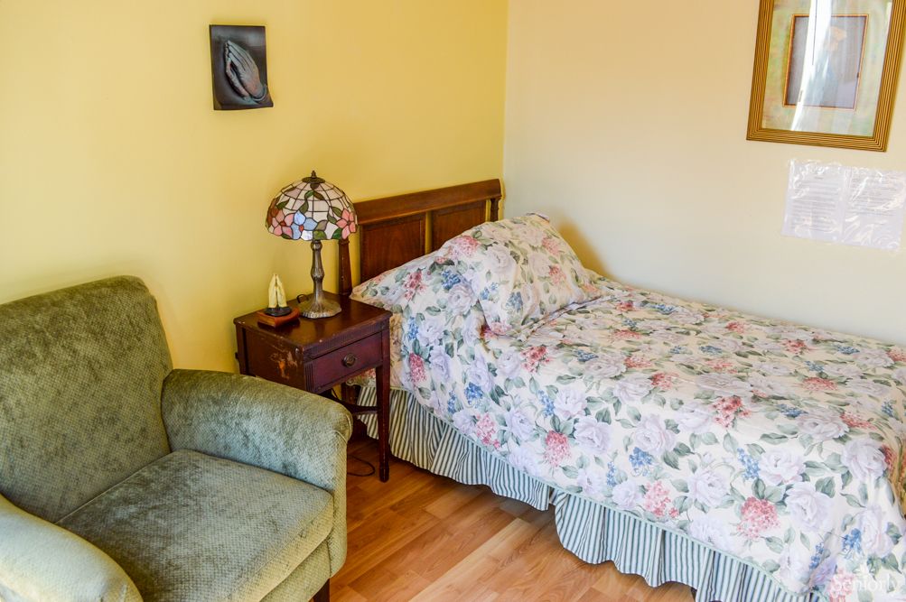 Cozy bedroom with a floral-patterned single bed, an armchair, and a decorative lamp on a nightstand.