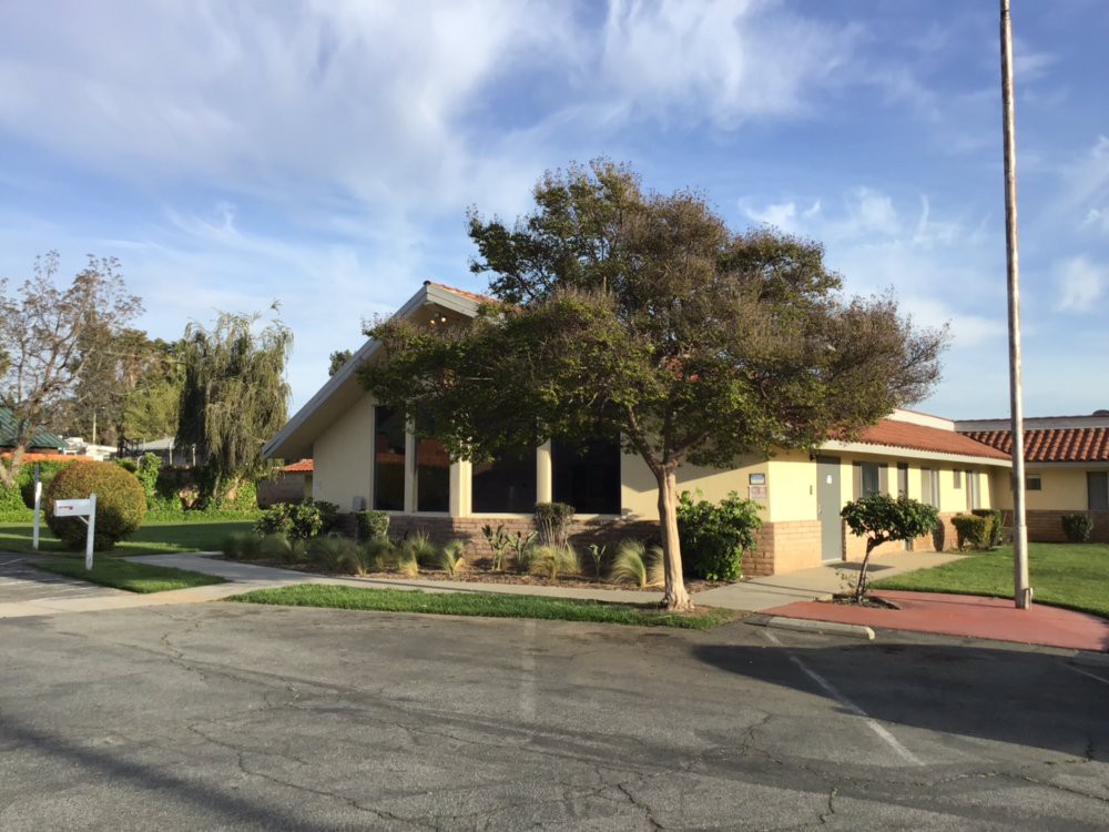 A suburban building on a street corner surrounded by trees under a partly cloudy sky.