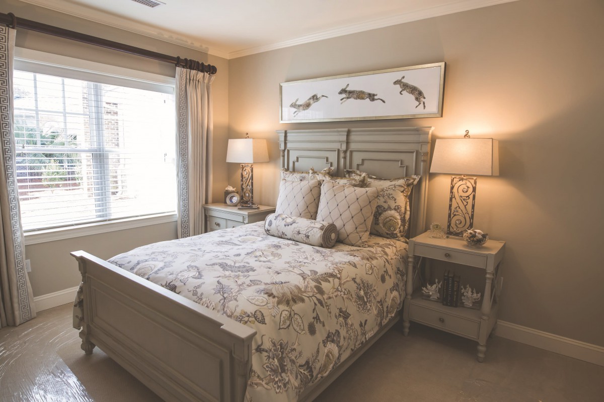 A cozy bedroom with a patterned bedspread, matching pillows, and wooden furniture, featuring bedside lamps and a large window.