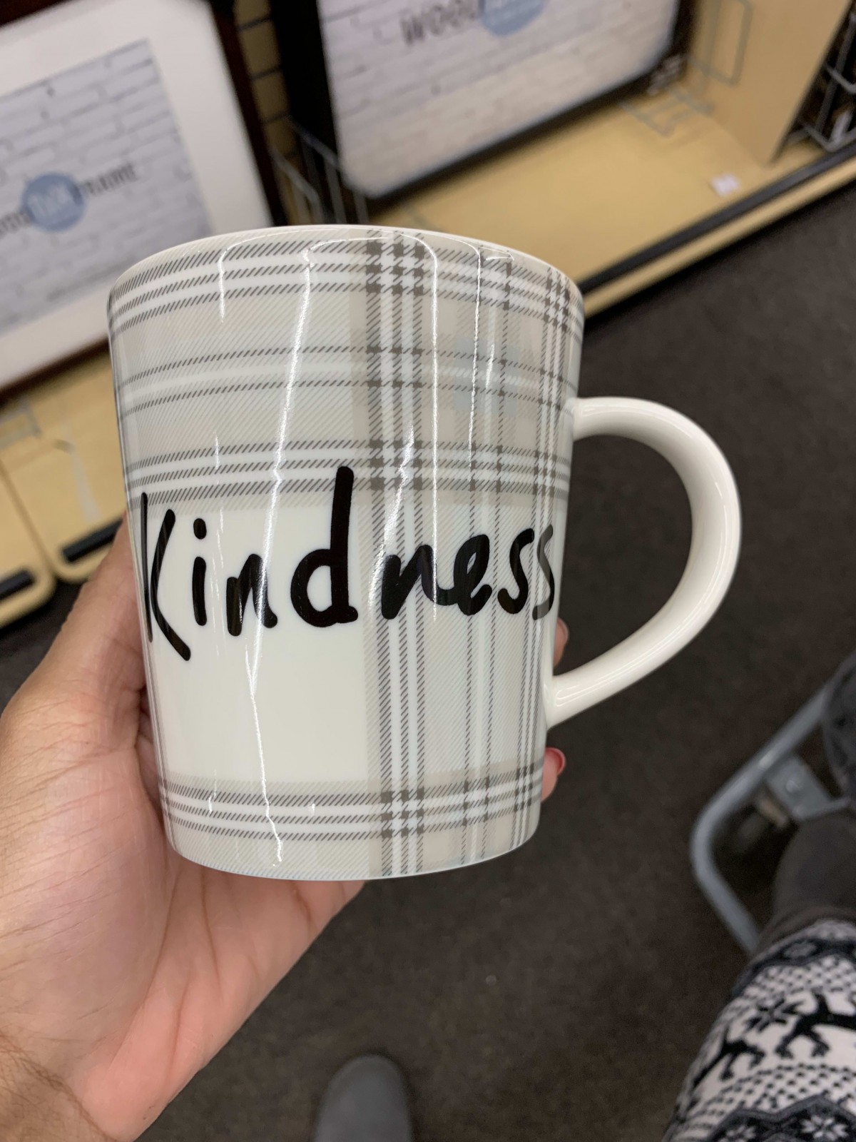 A ceramic mug with a plaid design featuring the word 'Kindness' in bold lettering.