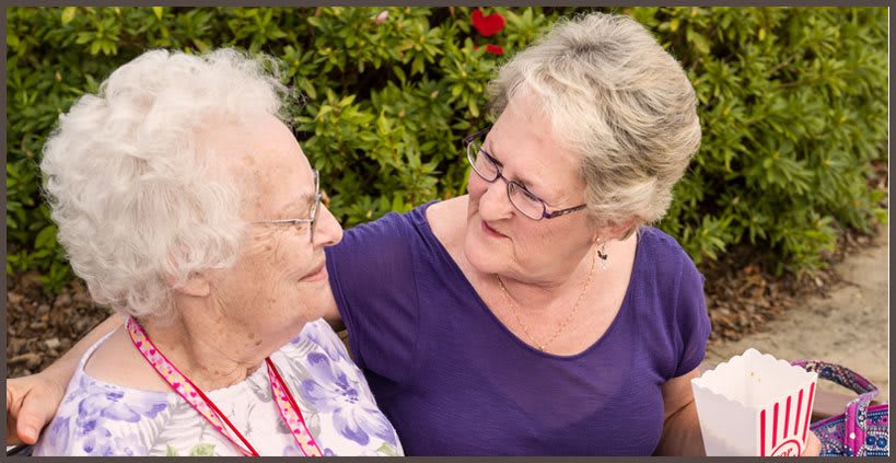 An elderly woman and another woman sharing a moment outdoors, exemplifying care and connection.