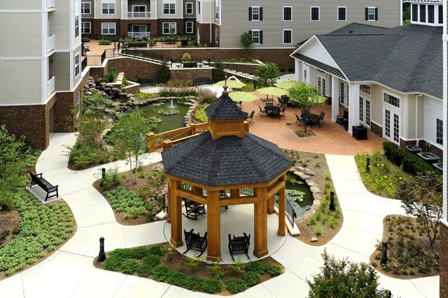 A beautifully landscaped garden featuring a wooden gazebo, surrounded by pathways and apartment buildings.