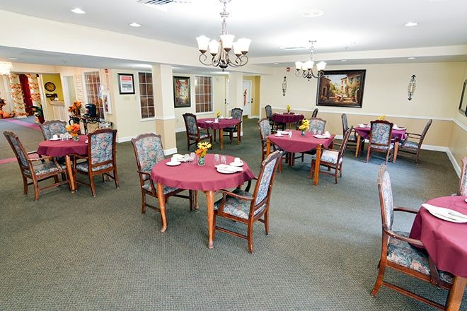 A well-set dining room with round tables, chairs, and chandeliers.