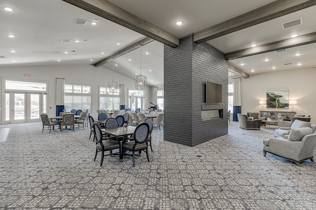 A modern dining area with elegant decor, featuring tables and chairs arranged around a central column with a mounted TV.