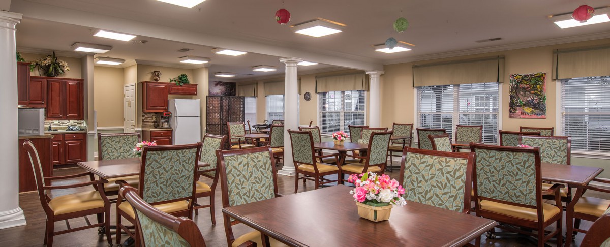 A well-lit dining area with arranged tables and chairs, featuring decorative flowers.
