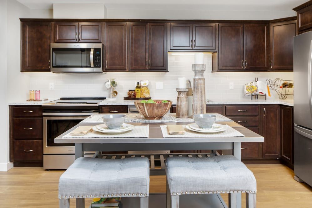 A modern kitchen with wooden cabinets and island seating, featuring stainless steel appliances.