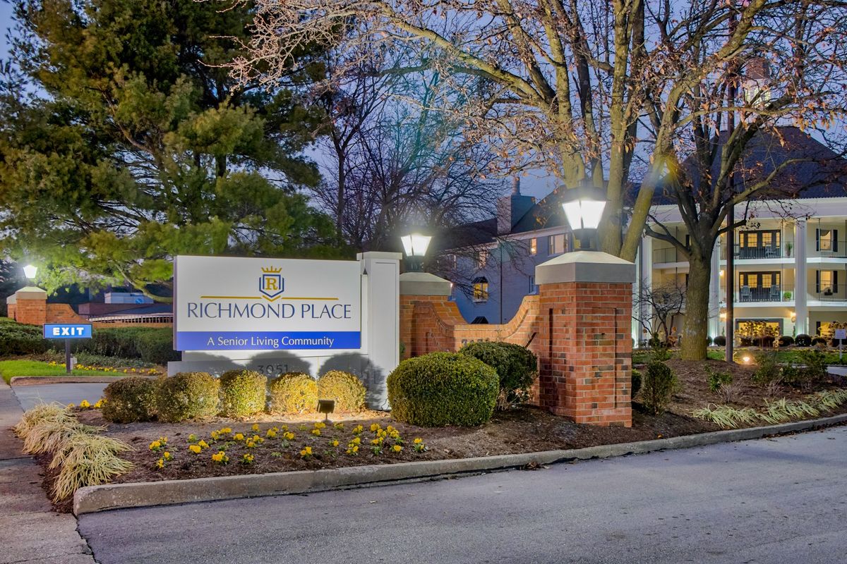 Entrance to an apartment complex with illuminated signage and landscaping at dusk.