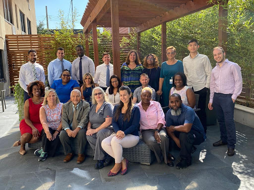 A diverse team gathering for a group photo in a sunny outdoor setting.