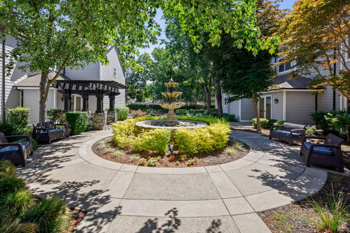 A scenic garden with a central fountain surrounded by trees and pathways.