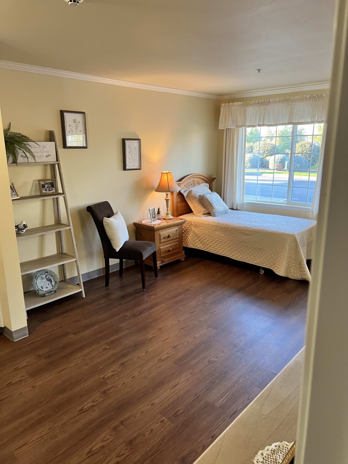 A cozy bedroom featuring a single bed, a bedside lamp, and a window with natural light.