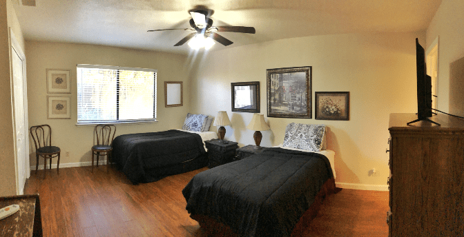 A cozy bedroom featuring two beds with black bedspreads, framed artwork on the walls, and a ceiling fan overhead.