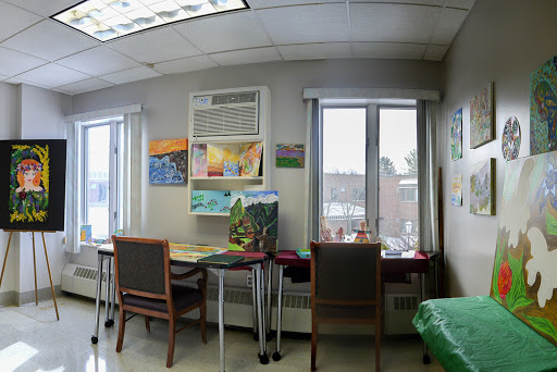 A cozy workspace with artwork on the walls, featuring tables and chairs near large windows.