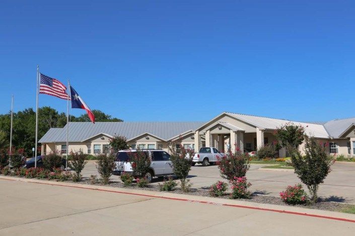 Exterior view of a building with cars parked in front and flags waving under a clear blue sky.