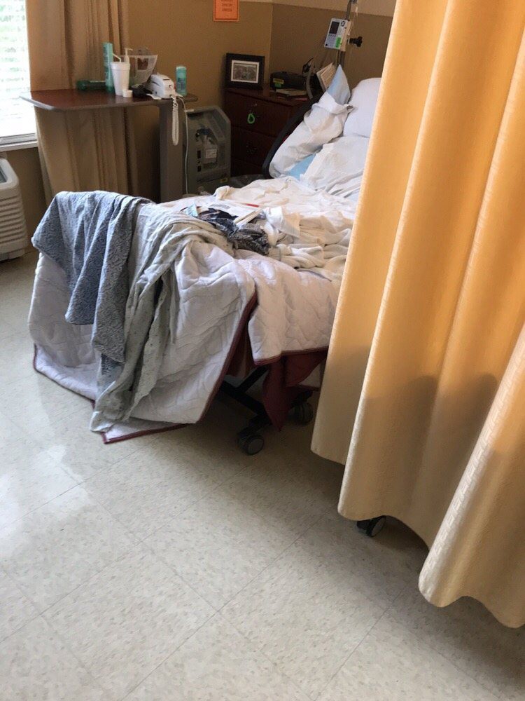 A hospital room with a bed, linens, and a privacy curtain.
