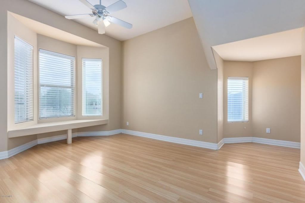 A bright, empty room with hardwood flooring and large windows letting in natural light.