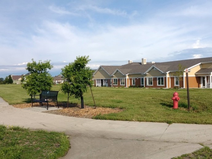 A wide view of a residential building with a lawn, trees, and a pathway leading to it under a cloudy sky.