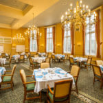 An elegantly decorated dining room with chandeliers and neatly set tables.