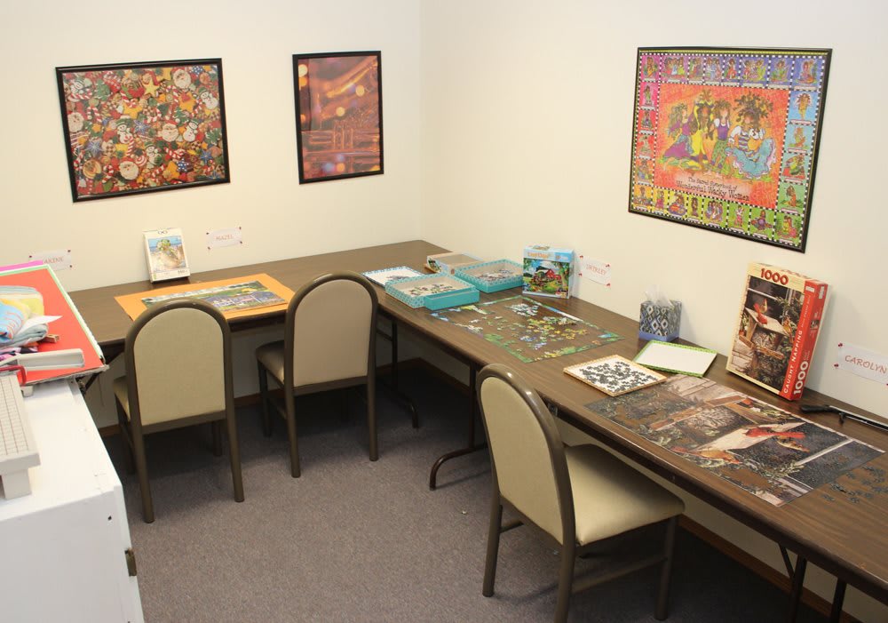 A room with tables and chairs set up for assembling jigsaw puzzles, decorated with colorful posters on the walls.