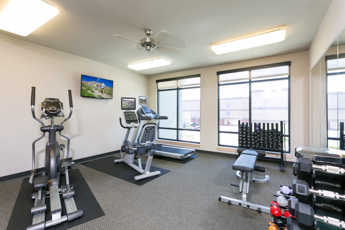 A well-equipped gym with various exercise machines and weights, brightly lit by natural light from large windows.