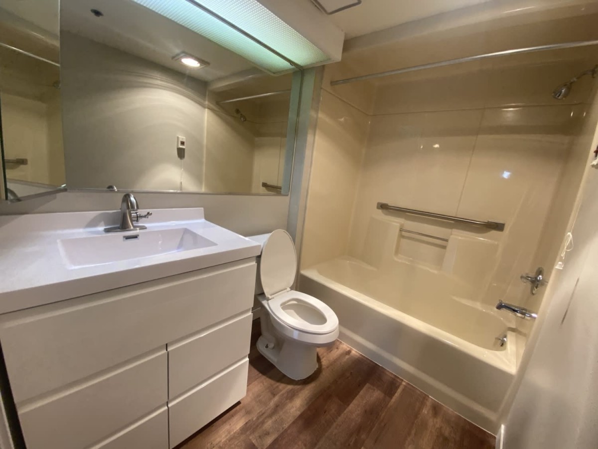 A modern bathroom featuring a toilet, sink, and bathtub with wooden flooring and ample lighting.