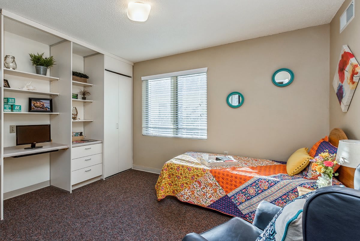 A cozy bedroom with a single bed adorned with colorful bedding, featuring built-in shelves and a window letting in natural light.