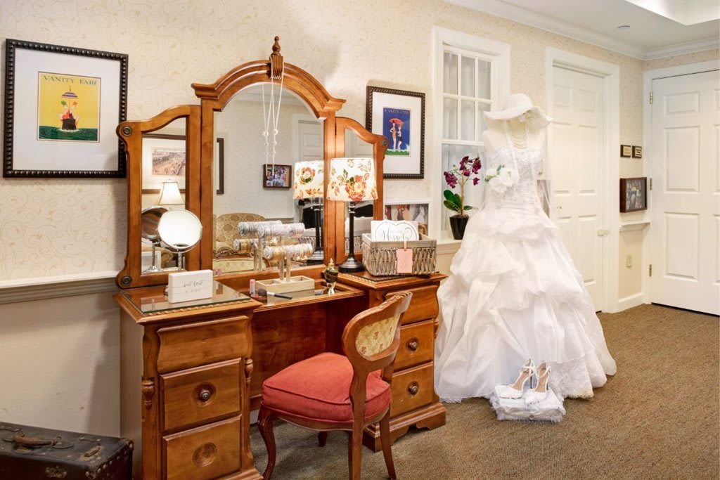 A vintage-style dressing room with a wooden vanity and a wedding dress on display.