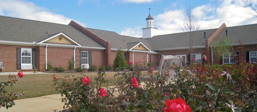 A picturesque brick building with a garden of red flowers under a blue sky.