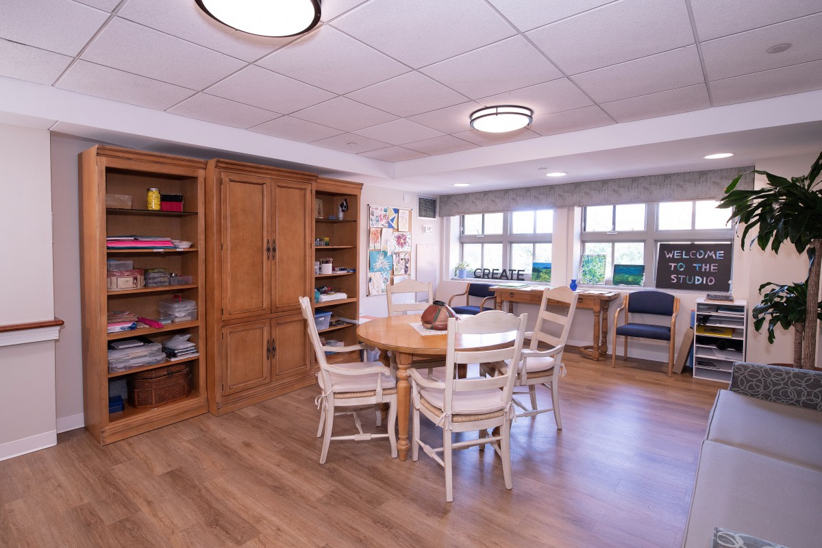 A cozy dining area with a wooden table and chairs, surrounded by shelves and large windows.