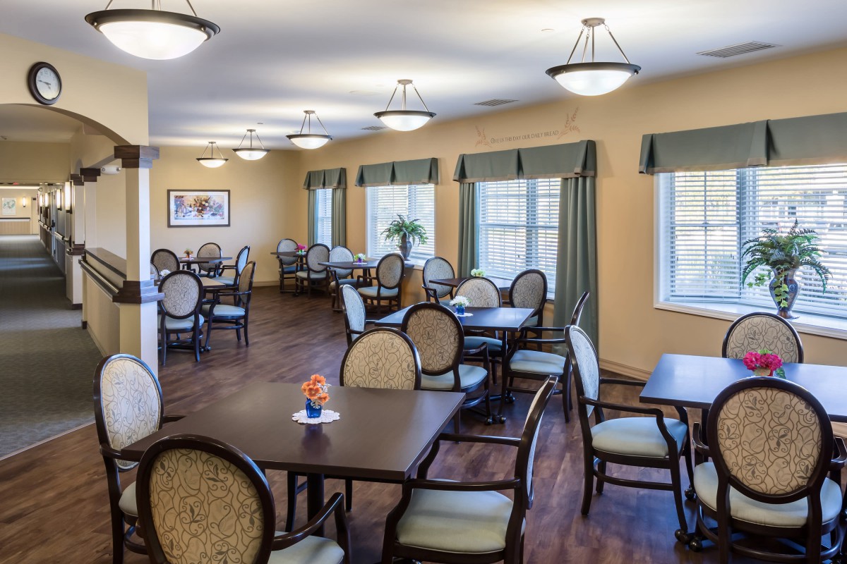 A well-lit dining area with multiple tables and chairs arranged neatly, featuring large windows with curtains.