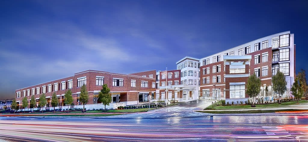 A modern brick building at night with illuminated windows and streaks of light from passing cars.