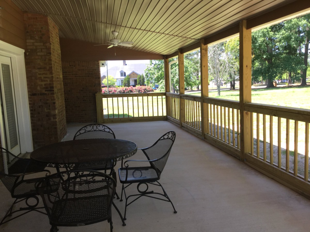A covered porch with iron furniture overlooking a garden.