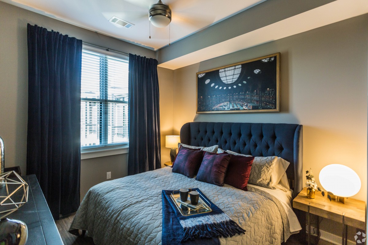 A cozy and stylishly decorated bedroom with a tufted headboard, dark curtains, and modern artwork.