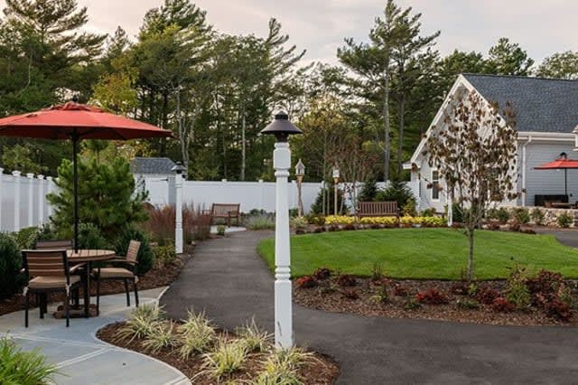 A beautifully landscaped garden with a paved pathway, lush green lawn, and decorative lamp posts.