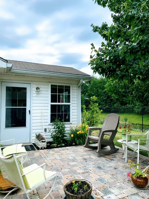 A cozy backyard patio with outdoor seating and lush greenery surrounding a small house.