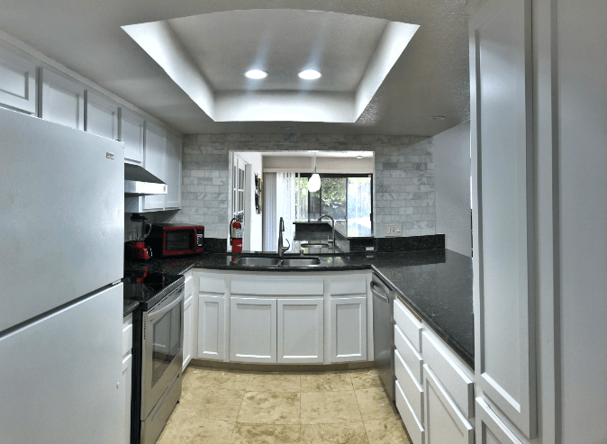 A modern kitchen featuring white cabinets and a black countertop with recessed lighting.
