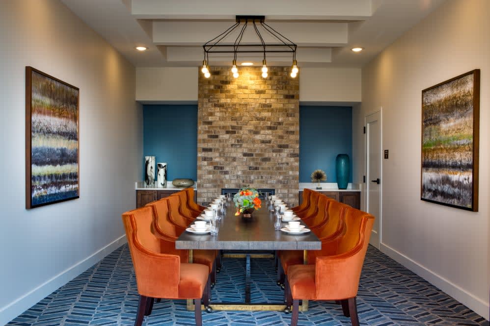 A modern dining room with orange chairs and a brick accent wall.