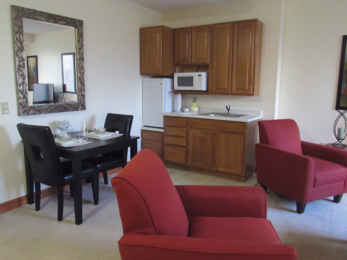 A cozy living space with a kitchenette, featuring red armchairs and a small dining area.