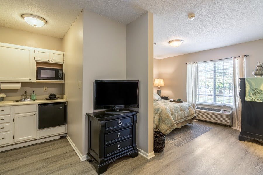 A cozy studio apartment with a combined living and sleeping area featuring a bed, television, and kitchenette.