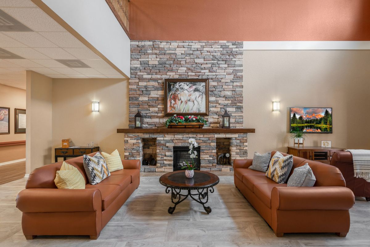A cozy living room featuring a stone fireplace, two orange couches, and a central coffee table.