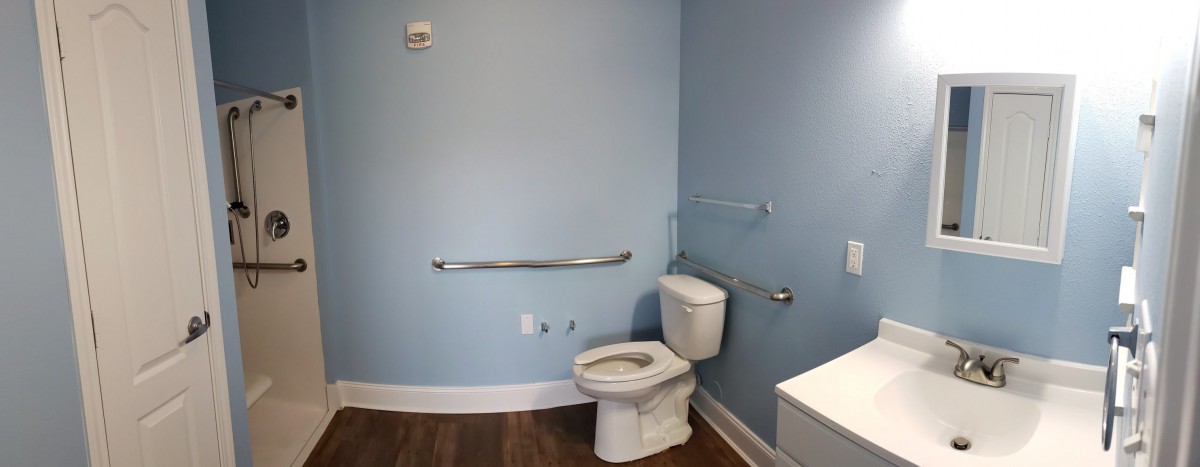 A bathroom with light blue walls, featuring a toilet and grab bars for accessibility.